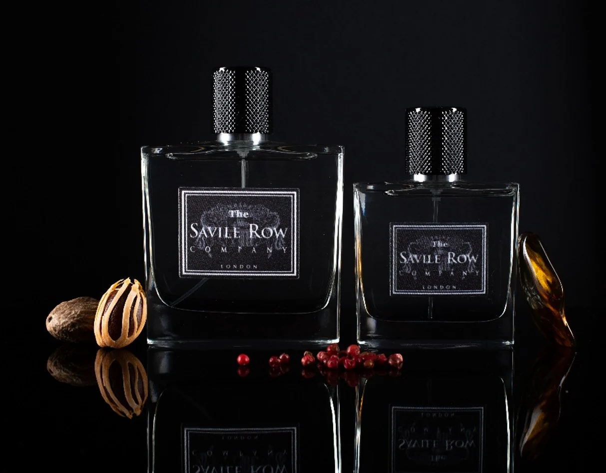 The Savile Row Heritage eau de toilette in both sizes, photographed on black with nutmeg and pink peppercorns