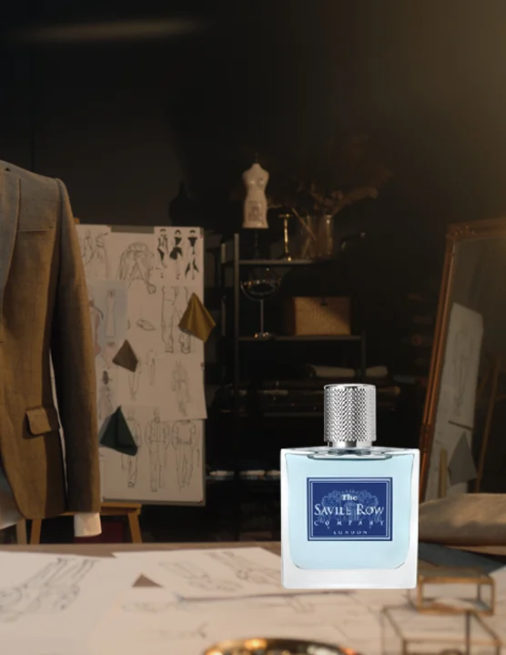 A Savile Row Mayfair eau de parfum on a tailor's workbench, design sketches and a jacket behind it
